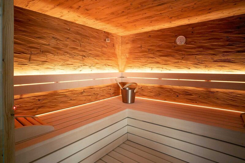 Die Sauna ist mit hellen Sitzbänken und dunkler Thermofichte gestaltet.