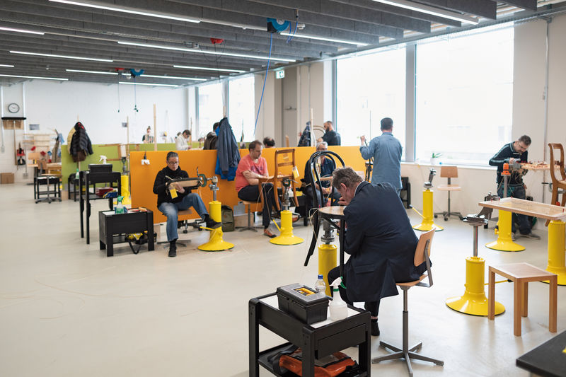 Die Werkstatt befindet sich in einem hellen Raum mit grossen Fenstern. Zwei Dutzend Mitarbeitende sitzen hinter ihren Werkstücken.