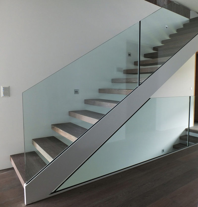 Gerade Holztreppe, deren Stufen mit Wandbolzen befestigt sind und von einer Stahlwange mit Glasbrüstung getragen werden. Ambauen.