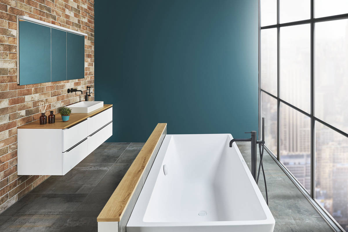 Die Wandkeramik in Backsteinoptik trifft auf warme Holzdetails und ein geradliniges Design von Badewanne und Waschbecken. Sabag.